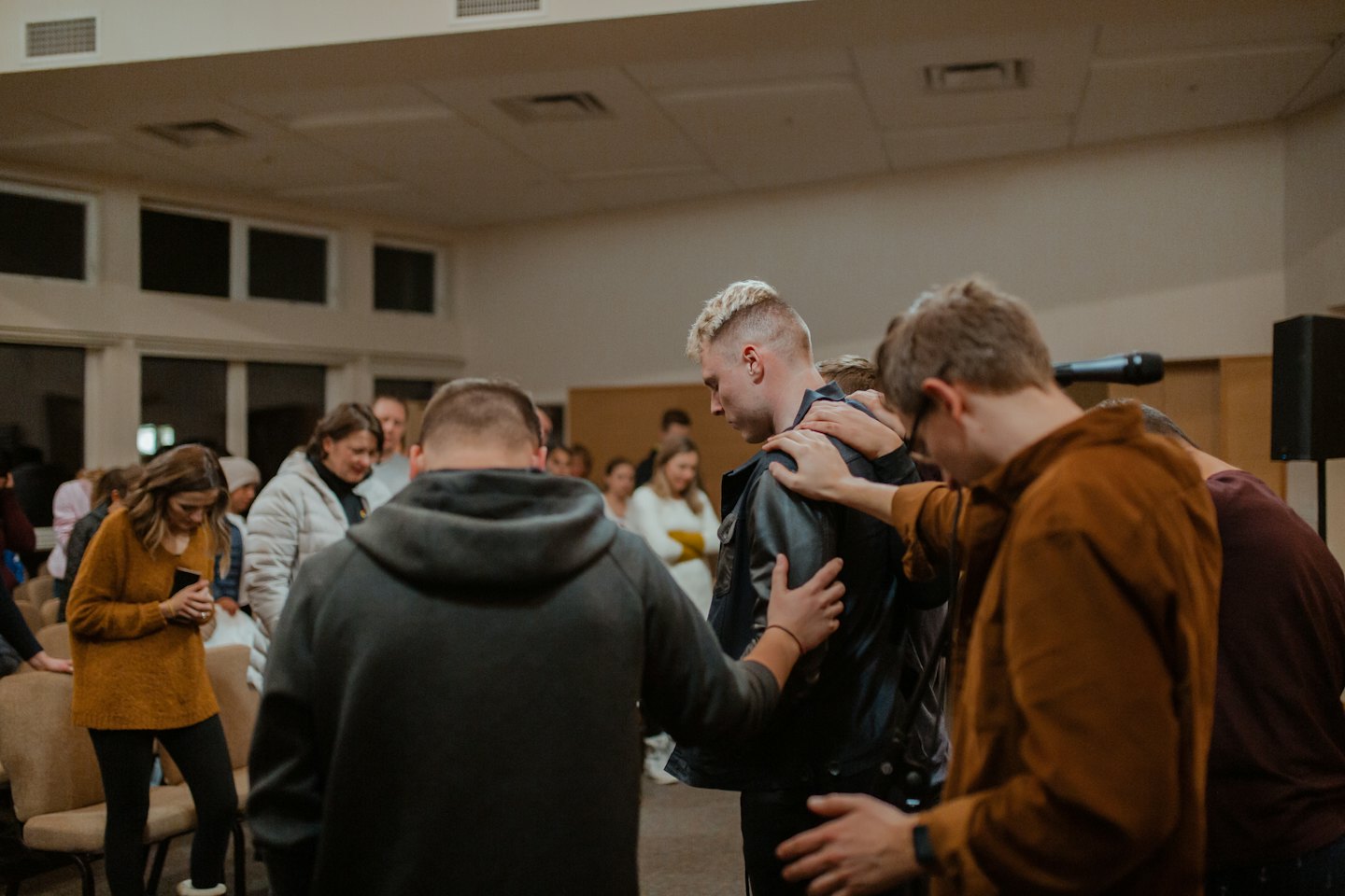 Adults placing hands on a young man during a prayer gathering.