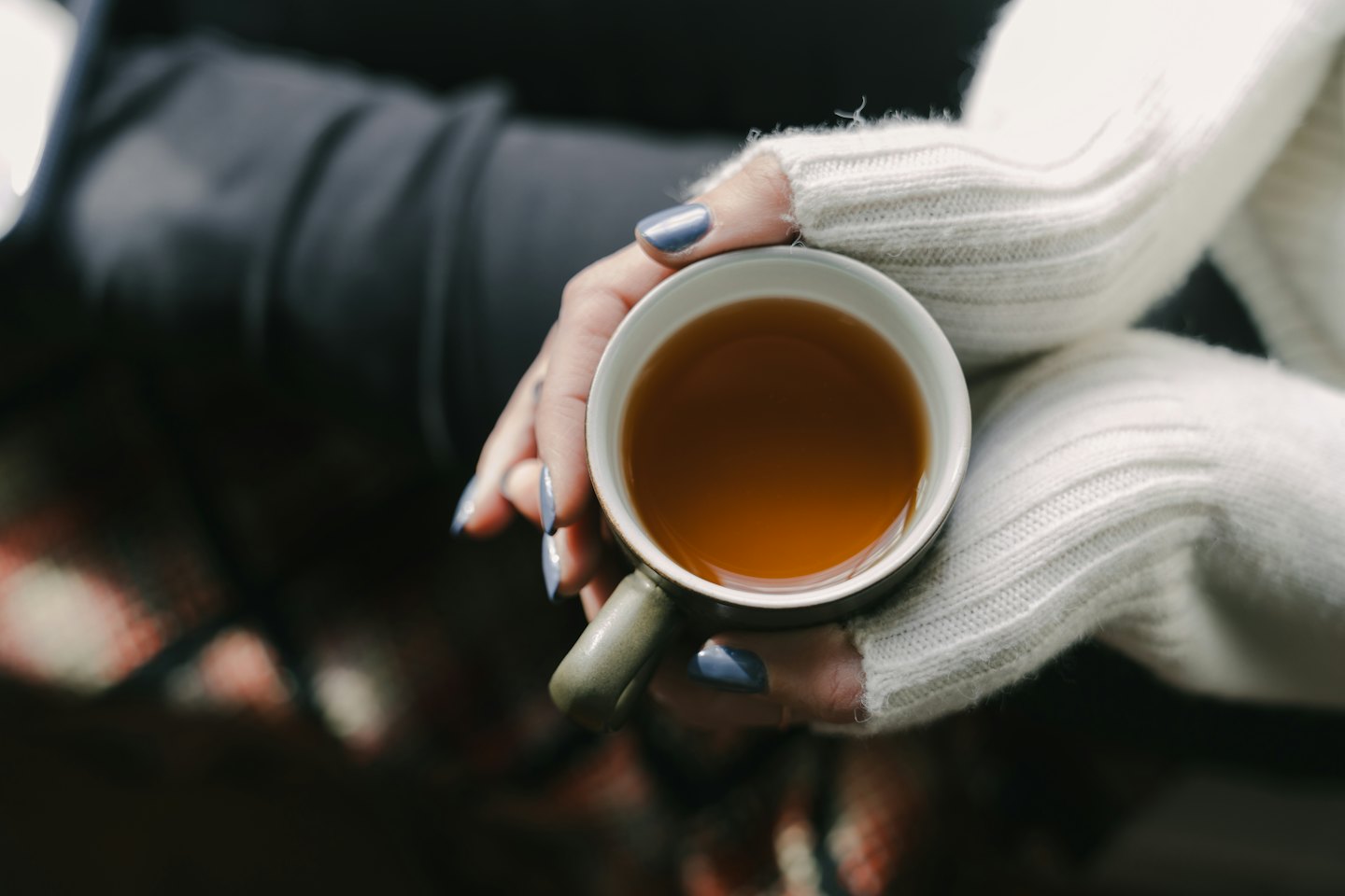 Hands holding a green mug of amber tea.