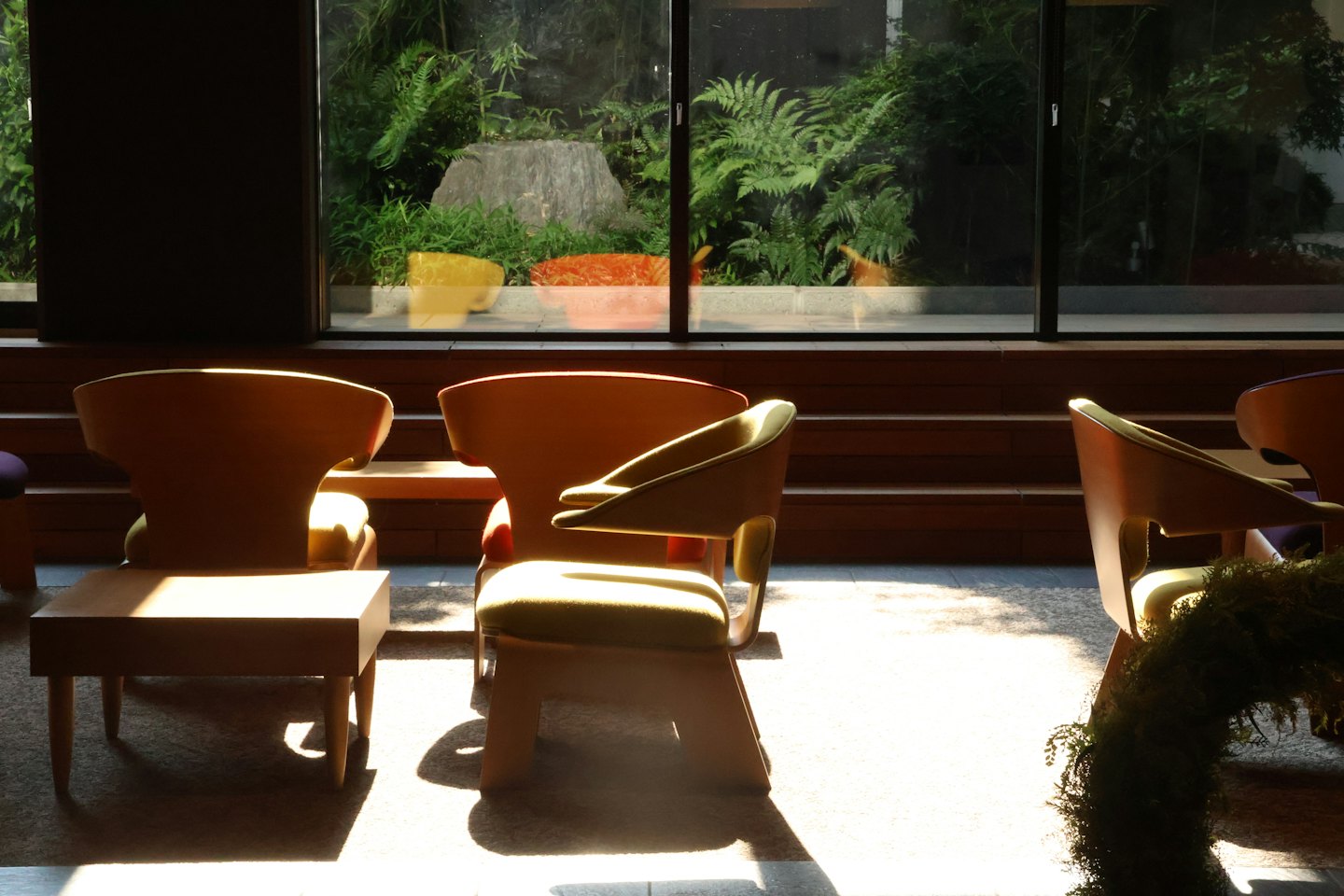 Modern wooden chairs with green cushions face a garden view.