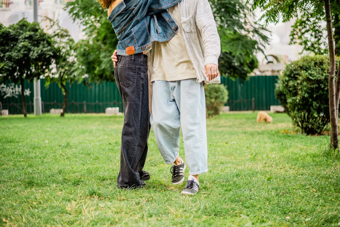 Two people wearing denim jeans embrace on a grassy lawn.